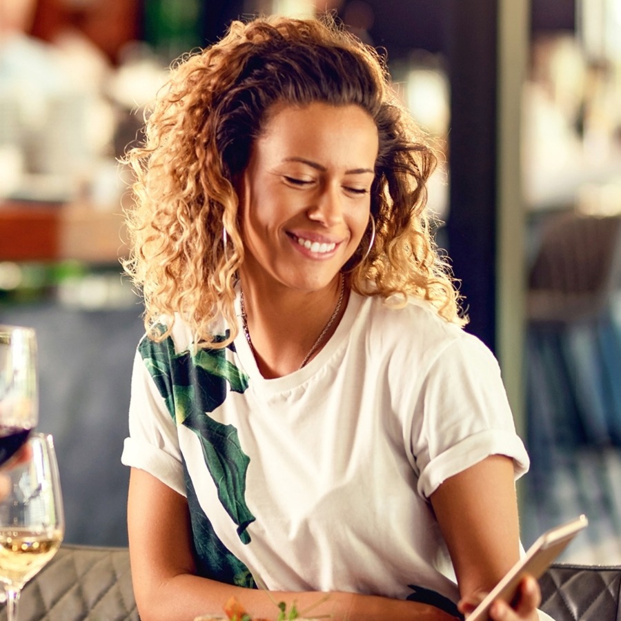 Frau mit Locken sitzt im Restaurant und bestellt lächelnd auf ihrem Smartphone
