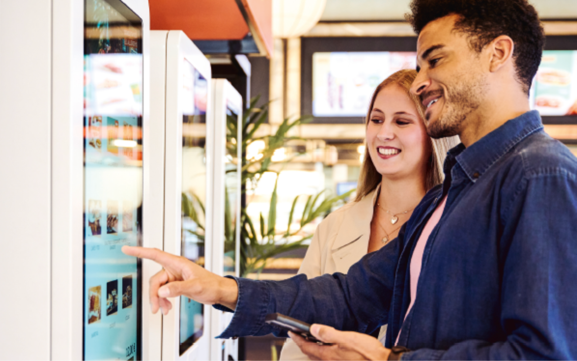 Mann und Frau bedienen lächelnd Self Service Terminal